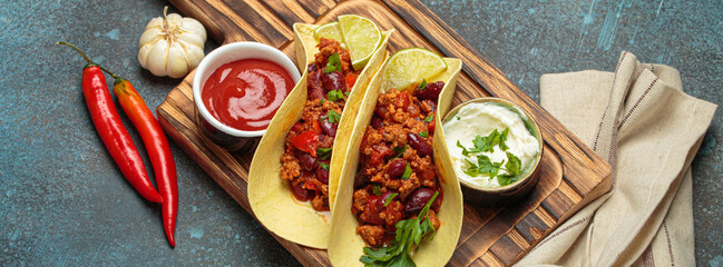 Delicious tacos with chili con carne, beans, parsley, lime, sour cream, and tomato sauce on a wooden board, a vibrant mexican culinary experience