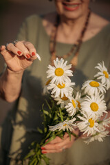 Portrait of a joyful elderly woman holding a bouquet of flowers. Old wrinkled hands with flowers in their palms close-up.