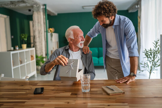 Adult son giving gift to senior father at home - Powered by Adobe