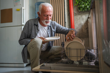 Elderly man loading dishwasher in modern kitchen
