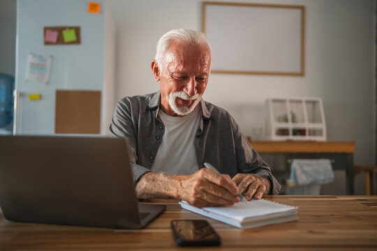 Focused senior freelancer working from home office reading notes