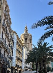 Central square in the historic center of Valencia, Spain. Valencia Cathedral through palm trees against blue sky on a sunny day in Queen's Square, Plaza de la Reina