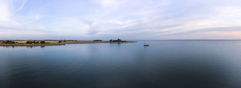 Tranquil evening panoramic aerial view of a tjalk ship with furled sails nestled on Markermeer lake near a rural village Schellinkhout in the Netherlands, surrounded by serene water and a calm horizon