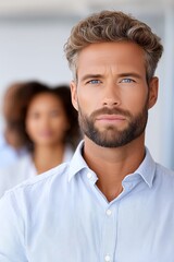 Fototapeta premium Confident man with beard and blue eyes in light shirt standing indoors with blurred people in background, symbolizing leadership, responsibility, teamwork, career growth, and business success