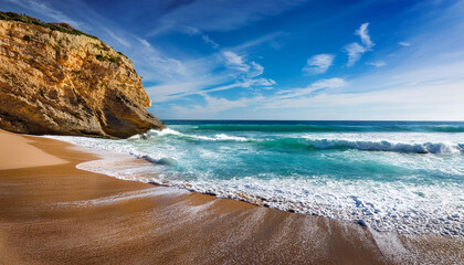 serene beach with waves and rocky cliff under a blue sky