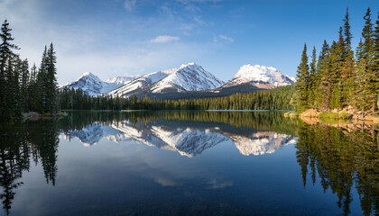 a tranquil lake reflecting snow capped mountains in the distance with pine trees framing the scene the calm water captures the serene beauty of the environment in perfect symmetry