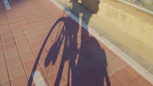 A shadow of a cyclist riding a bicycle captured during golden hour. The moving shadow and the soft light create a dynamic and artistic perspective on a textured surface.
