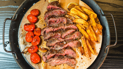 Juicy sliced medium rare ribeye steak served on a wooden board with crispy homemade fries, roasted garlic, fresh thyme, and cherry tomatoes. Perfect for food blogs and menus.