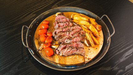 Juicy sliced medium rare ribeye steak served on a wooden board with crispy homemade fries, roasted garlic, fresh thyme, and cherry tomatoes. Perfect for food blogs and menus.