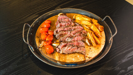 Juicy sliced medium rare ribeye steak served on a wooden board with crispy homemade fries, roasted garlic, fresh thyme, and cherry tomatoes. Perfect for food blogs and menus.