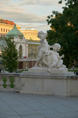Obraz premium Sculpture of two infant cherubs in Vienna’s Palm House garden, highlighting detailed craftsmanship, classical design, and serene outdoor ambiance.