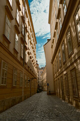 Narrow Viennese street with historic yellow building facades, cobblestone road, and bright blue sky with clouds, showcasing classic European urban charm.