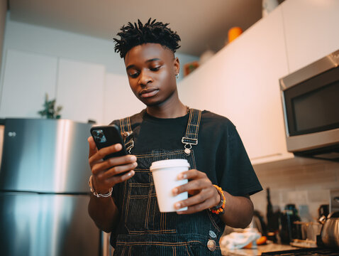 Young man using smartphone and drinking coffee in kitchen