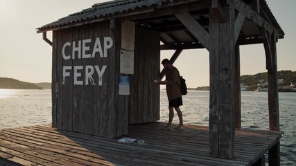 Tourist purchasing a ticket at a budget friendly ferry booth on a wooden pier during a picturesque sunset, highlighting the serene evening atmosphere