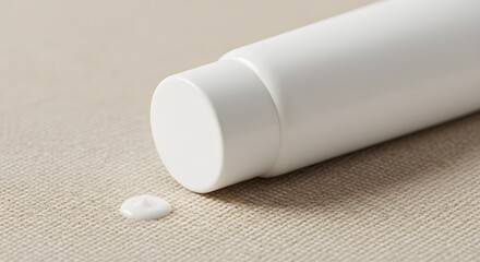 A close-up shot of a sleek white cosmetic tube resting on a soft beige fabric surface, with a small dollop of product beside it. The smooth, minimalist design of the tube is highlighted by the soft li