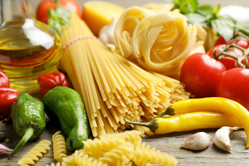 Different types of pasta and ingredients on wooden table, closeup