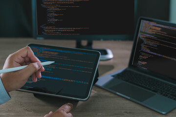 Close-up of programmer freelance working on tablet and laptop with code on screen, modern software development, coding, and remote work in home office environment.