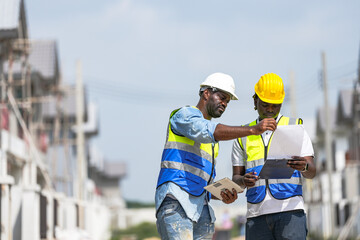 An experienced construction foreman mentors a young apprentice on a building site. The senior engineer uses a tablet to explain project details, providing on-the-job training and guidance.
