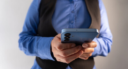 Close-up of a smartphone held by a person wearing a blue blouse and black vest
