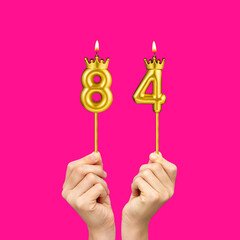 Birthday on a fuchsia background with the number 84 - Hands holding number-shaped candles