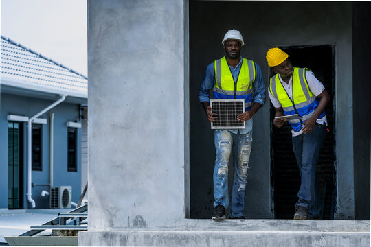 Engineers on a construction site inspect a solar panel, discussing its placement on the building's exterior. A focus on sustainable installation, energy solutions, and project execution.