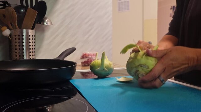 Close-up of woman slicing kohlrabi (cabbage turnip) in her cozy kitchen, preparing a healthy meal. Everyday life, home cooking and fresh vegetables in focus