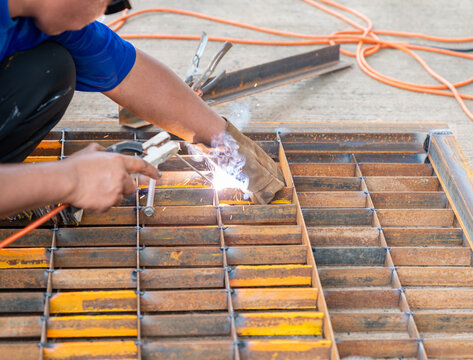 A worker is welding a steel grate cover for a drainage channel.