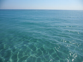 Crystal clear turquoise ocean water shimmering under bright sunlight with gentle ripples and serene horizon