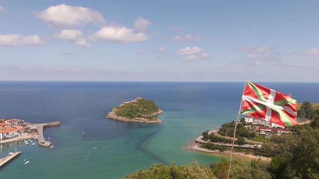 Basque flag flying proudly above Lekeitio coast with San Nicolas island and turquoise sea