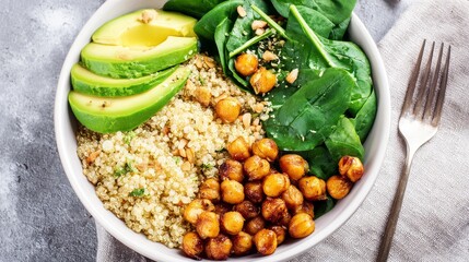 Healthy vegan bowl with quinoa, avocado slices, roasted chickpeas and spinach leaves, colorful nutritious ingredients in bright daylight, top-down view, wellness lifestyle concept