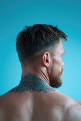 Naklejka premium Stylish man showcasing intricate back tattoo against vibrant blu