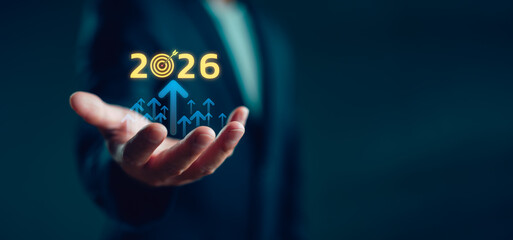 Businessman holding virtual 2026 with rising arrows and target icon, symbolizing new year business goals, strategic vision, future growth, success planning and performance improvement.
