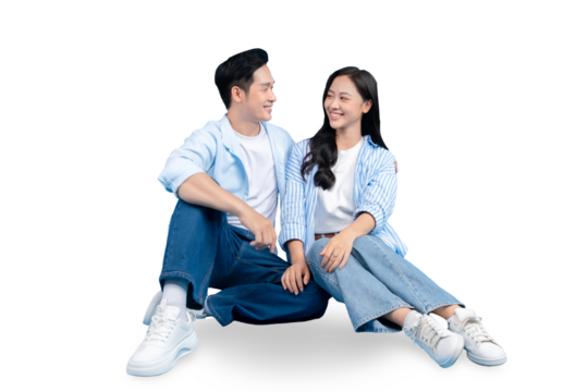 A young couple smiles and looks at each other lovingly while sitting, wearing light blue tops and jeans against a PNG background.