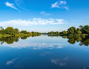 Obraz premium A serene body of water, reflecting the vibrant blue sky above, surrounded by lush greenery and distant mountains, creating a tranquil natural scene.