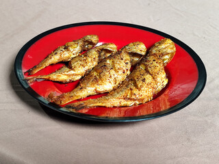 Four crispy, golden fried fish served on a red plate with black lines.
