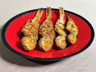 Four crispy, golden fried fish served on a red plate with black lines.