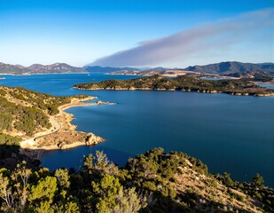 Obraz premium A serene lake nestled amidst lush green trees and majestic mountains, reflecting the vibrant blue sky and fluffy white clouds above.