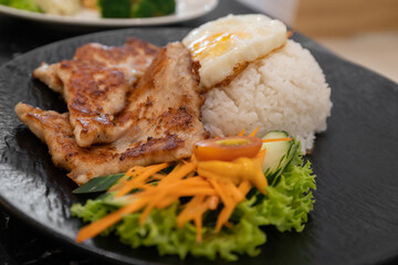 A plate featuring grilled pork chops with white rice, fresh salad, and a sunny side up egg, beautifully arranged served on a sleek black plate.