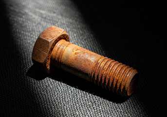 A single rusted bolt placed diagonally on dark linen, side-lit to reveal its corroded texture and aged patina.