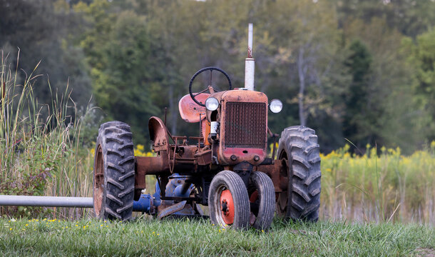 Old red vintage antique farming tractor parked in a rural grassy field
