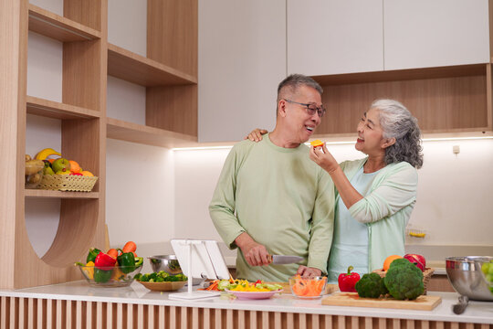 Older Asian couple prepares healthy meal together kitchen sharing food bonding happy moment senior lifestyle cooking nutritious dinner - Powered by Adobe
