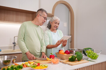 Older Asian couple preparing healthy food kitchen looking recipe digital tablet cooking lifestyle senior couple home meal prep together