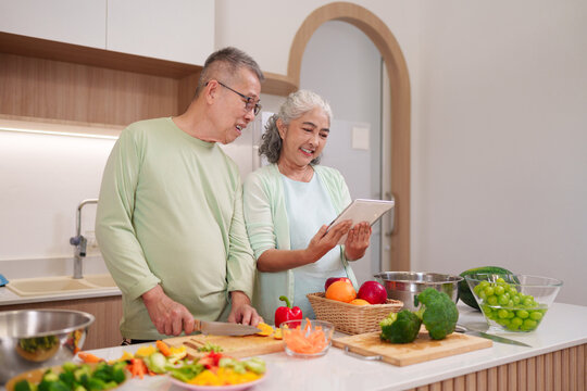 Older Asian couple preparing healthy food kitchen looking recipe digital tablet cooking lifestyle senior couple home meal prep together