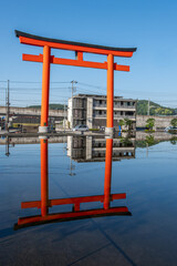 Traditional red torii gate reflected in calm water near urban buildings at Fujinomiya, Shizuoka, Japan,