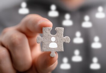 Hand holding a puzzle piece with a person icon, surrounded by other puzzle pieces