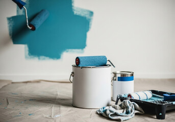 Home renovation project with teal paint roller and supplies on drop cloth