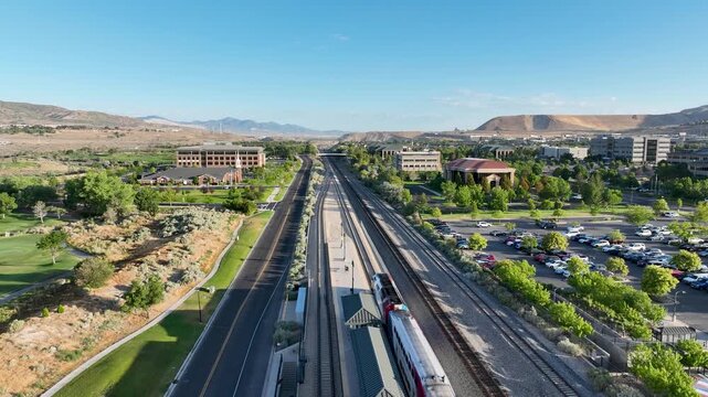 FrontRunner light rail commuter passenger train leaving Lehi Station in towards Provo - pullback aerial reveal on a sunny morning
