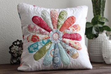 A handcrafted square throw pillow featuring a vibrant floral fabric pattern resting on a wooden surface