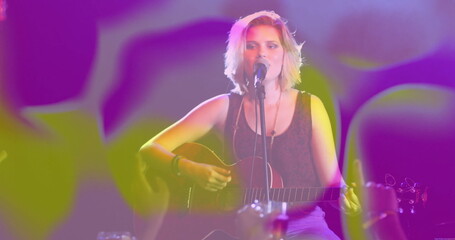 Strumming singer-guitarist with acoustic guitar in club, leaning into microphone under stage lights
