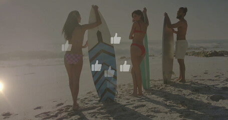Capturing three surfers wearing swimwear holding boards on beach at sunset showing thumbs up icons